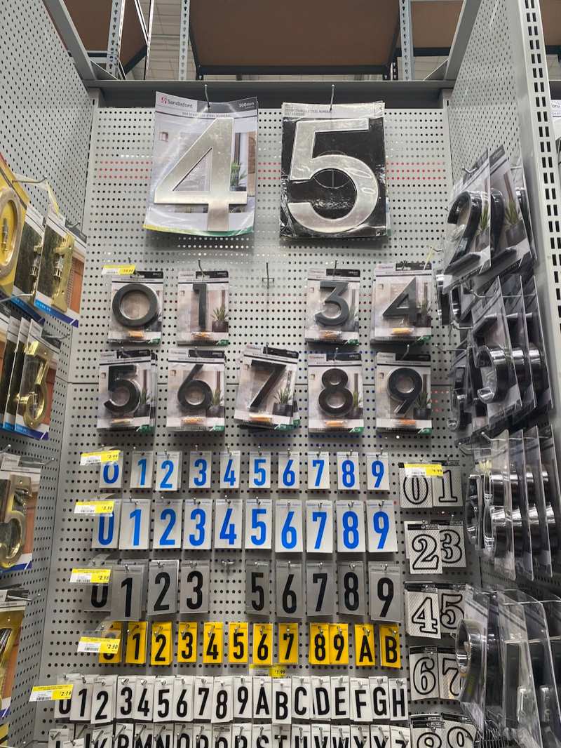 Hardware store pegboard display of house numbers in stainless steel, black aluminium and adhesive styles
