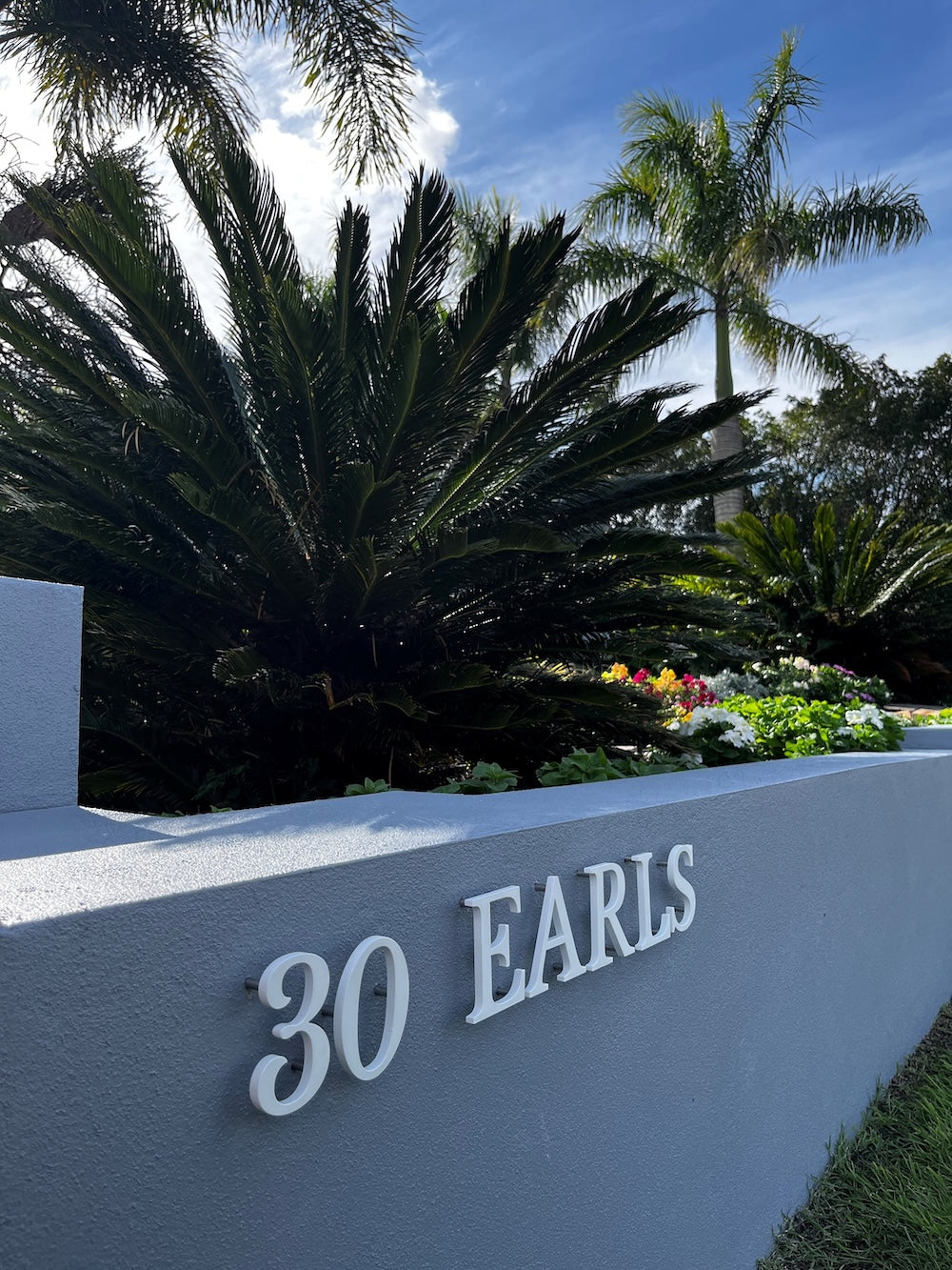 30 EARLS in matt white serif letters on a grey rendered wall, with cycads and palm trees behind