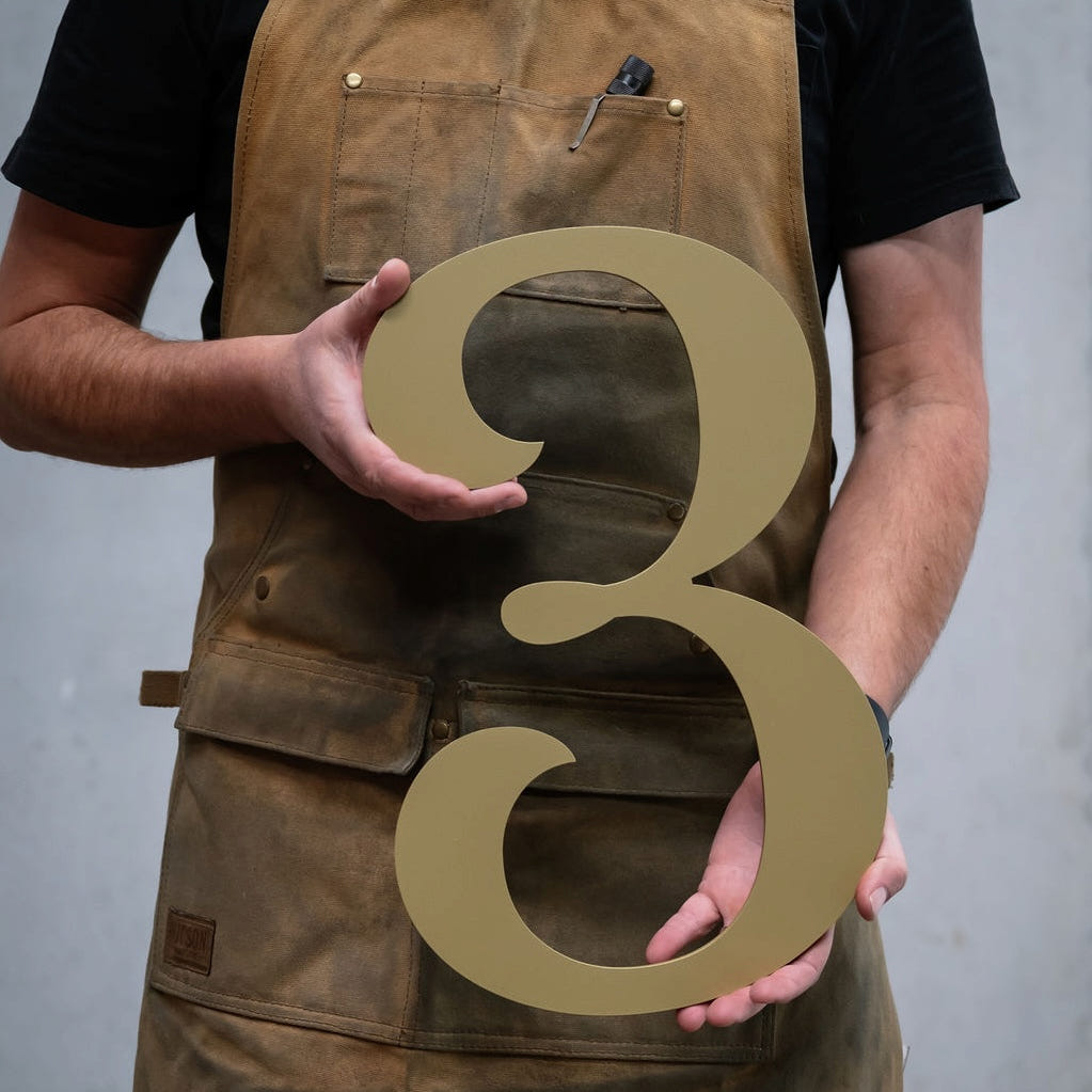 Maker holding a large custom house number 3 in brushed gold
