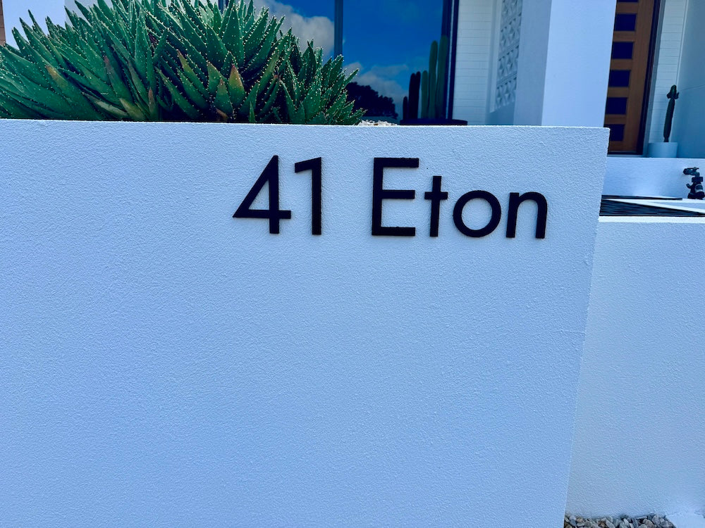 41 Eton in matt black letters on a white rendered letterbox wall, with succulents and a white house behind